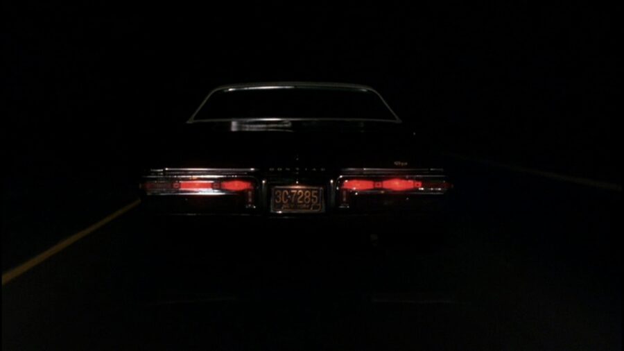 What is The Hollywood Model (aka "Berettermodellen")? Definition & Examples 4 Rear view of a black car driving down a dark highway with glowing red taillights