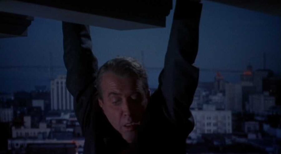 30 Films Every Budding Film Student Should Watch & Why 2 A man hangs from a rooftop ledge at night, with a city skyline and bridge in the background.