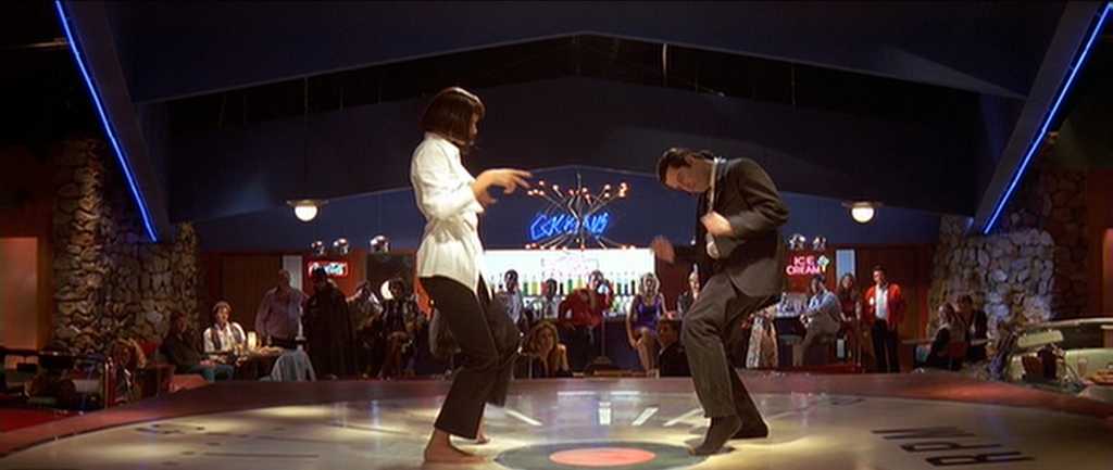 30 Films Every Budding Film Student Should Watch & Why 11 A man in a suit and a woman in a white shirt and black pants dance barefoot on a lit-up floor in a retro-themed restaurant.