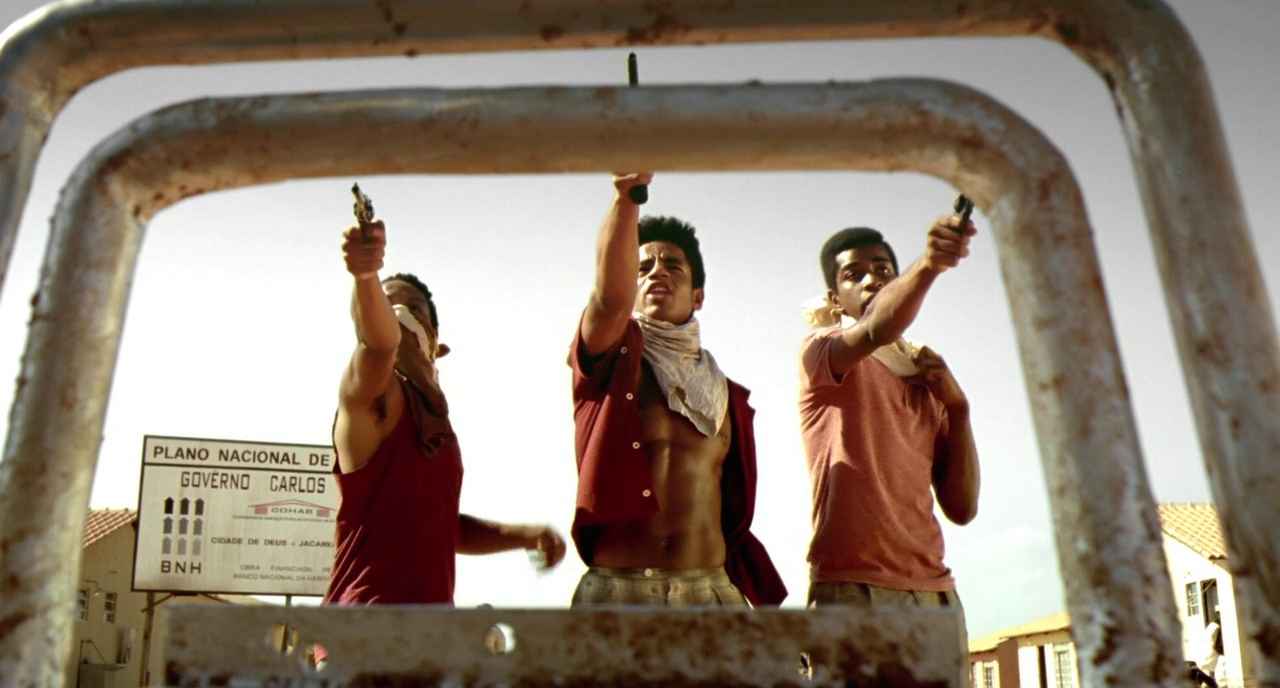 30 Films Every Budding Film Student Should Watch & Why 15 Three young men aim pistols while standing in the street, framed through a rusted metal gate.