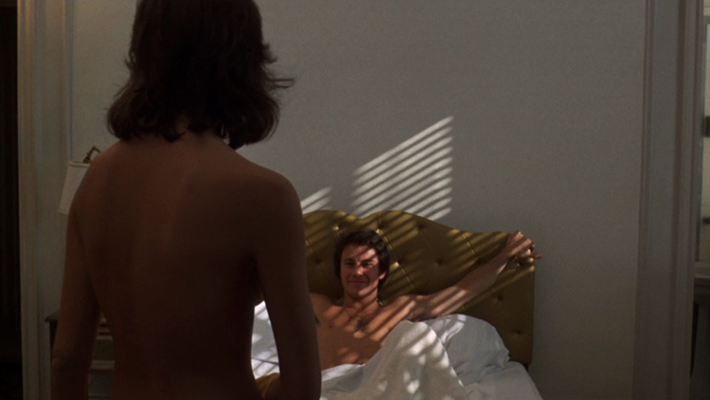 30 Films Every Budding Film Student Should Watch & Why 9 A shirtless man lies in bed, smiling at a topless woman standing in the foreground, with sunlight streaming through blinds.