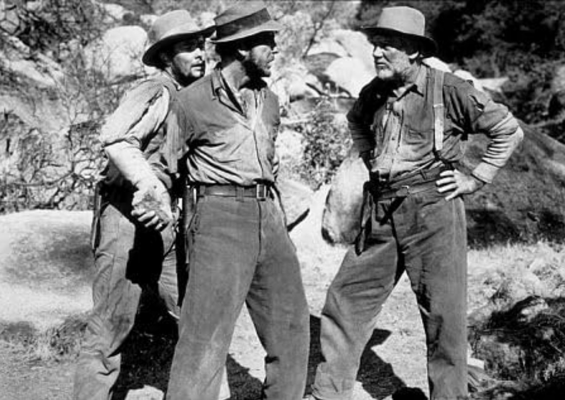30 Films Every Budding Film Student Should Watch & Why 20 Three men in worn work clothes and hats stand in a rocky outdoor setting, two facing off while the third looks on tensely.