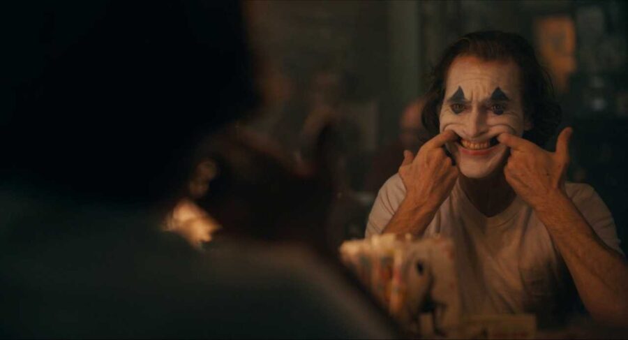 30 Films Every Budding Film Student Should Watch & Why 19 A man in clown makeup sits at a mirror, using his fingers to pull his mouth into a forced smile.