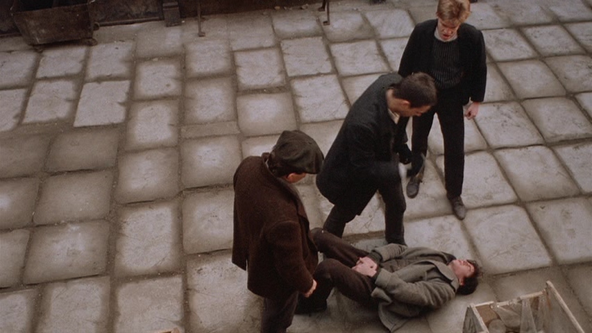 10 Best Gangster Movies of All Time For Filmmakers To Watch 6 Three boys stand over another boy lying on the ground in a rough courtyard setting