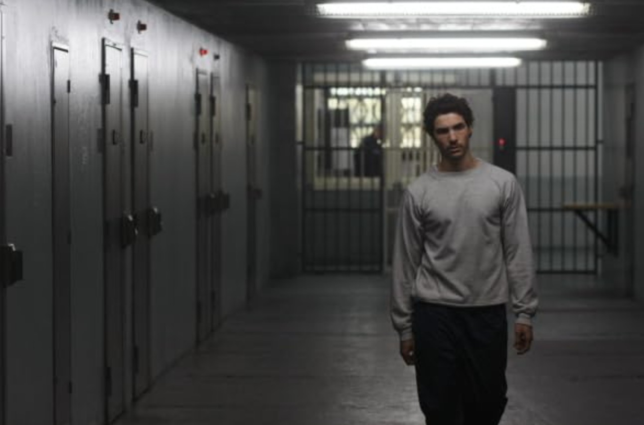 10 Best Gangster Movies of All Time For Filmmakers To Watch 11 A young man in a gray sweatshirt walks alone down a dim prison hallway with barred doors
