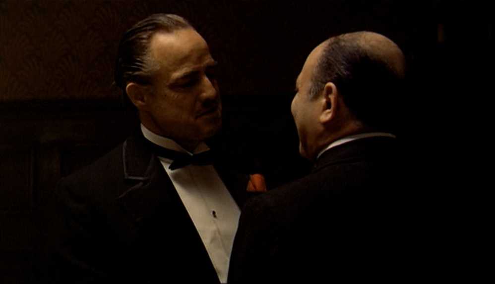 10 Best Gangster Movies of All Time For Filmmakers To Watch 2 Don Vito Corleone listens to a man whispering in his ear in a dimly lit room