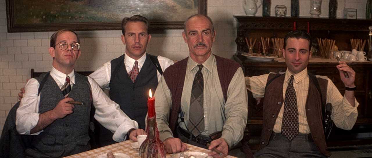 10 Best Gangster Movies of All Time For Filmmakers To Watch 8 Four men in vests sit at a table with a red candle, armed and serious but relaxed