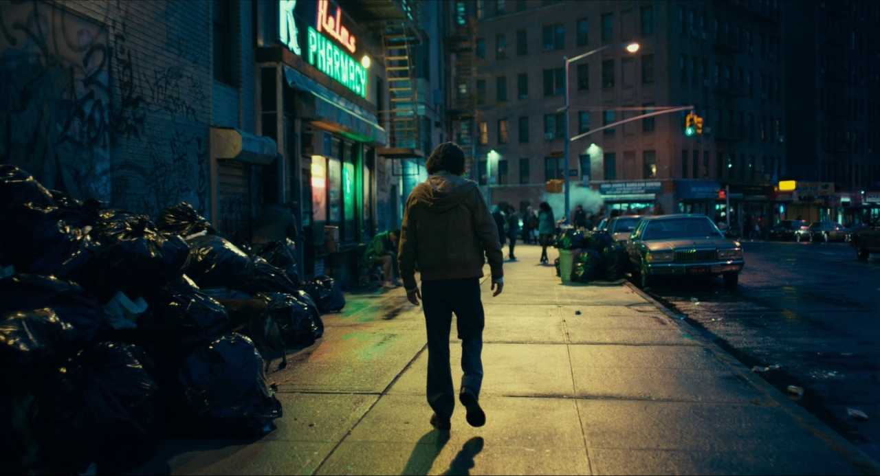 Context in Screenwriting and Film: A Complete Guide 6 A man walks down a dark city sidewalk lined with overflowing garbage bags, neon signs, and old cars