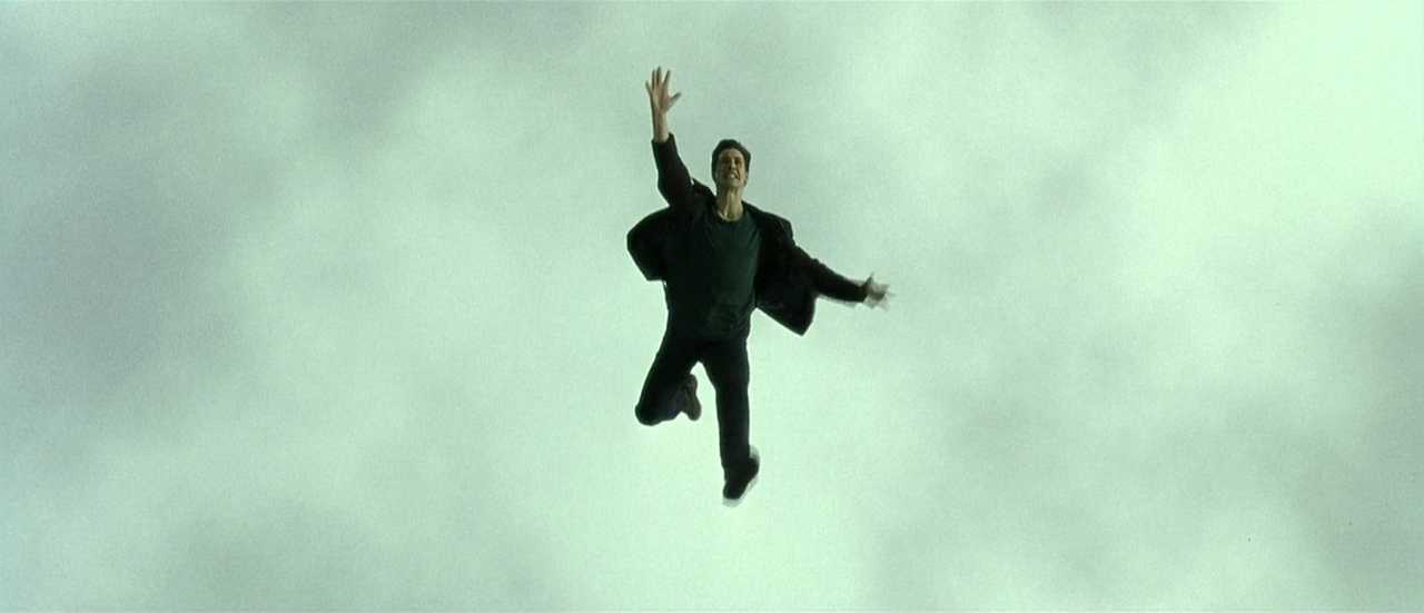 What is Campbell's Monomyth? A Hero Guide for Filmmakers 8 Neo falls through the air mid-jump, reaching upward, framed against a pale cloudy sky.