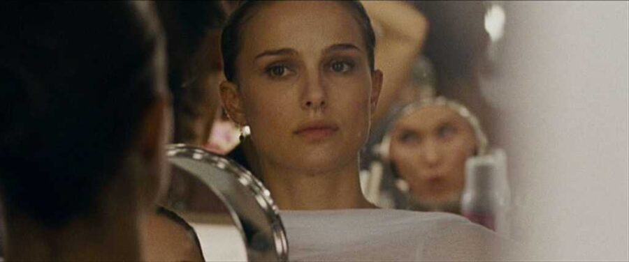 Black Swan (2010) hamartia example image Nina Sayers looks into a mirror with a tense, focused expression in a dressing room.