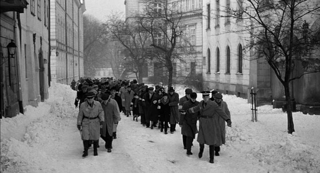 What Is the Setting in Film? Time, Place & Mood 4 Prisoners and Nazi officers move through snowy streets between tall buildings in a black-and-white wartime scene.