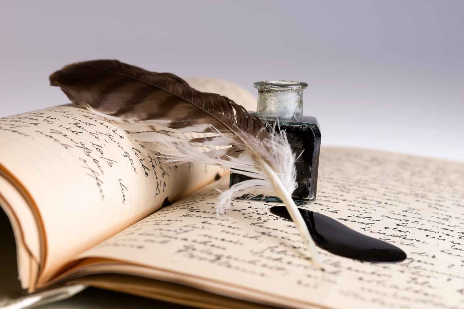 Quill, ink, and handwritten pages A feather quill lies across open handwritten pages beside a small ink bottle and a dark ink spill.