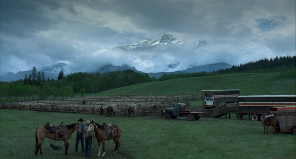 What Is the Setting in Film? Time, Place & Mood 3 Two men stand beside horses in a wide grassy field with trucks and snowy mountains under heavy clouds.