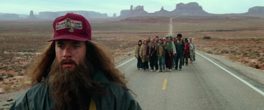 Forrest Gump during his cross-country run (1994) Forrest Gump stands on a desert road with a long beard and a Bubba Gump cap, while a small group of followers stands behind him.