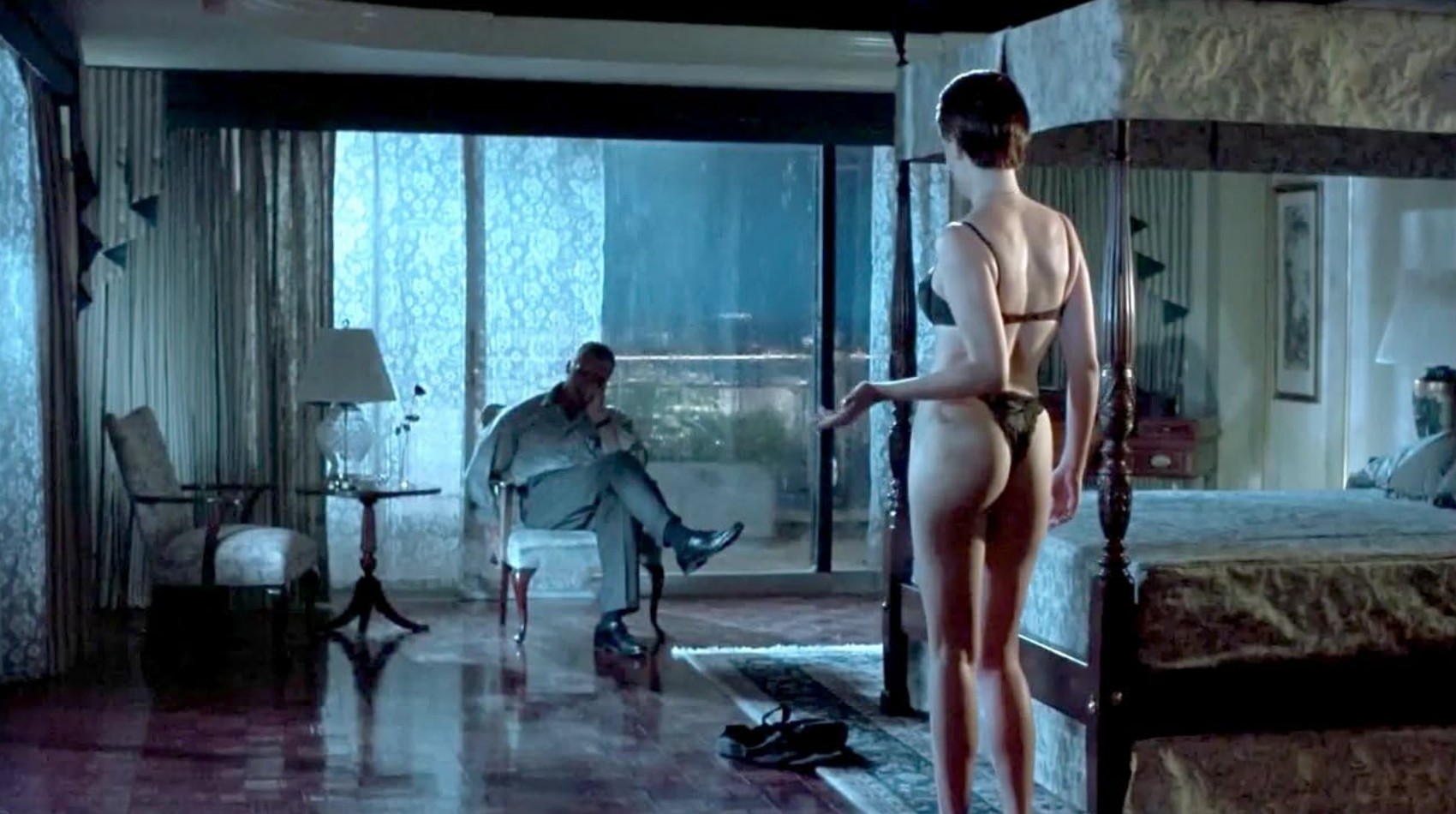 Oxymoron Definition: Examples in Film and Literature 2 A woman in lingerie stands near a bed, facing a man seated in a chair across the room, with rain outside the glass windows behind him