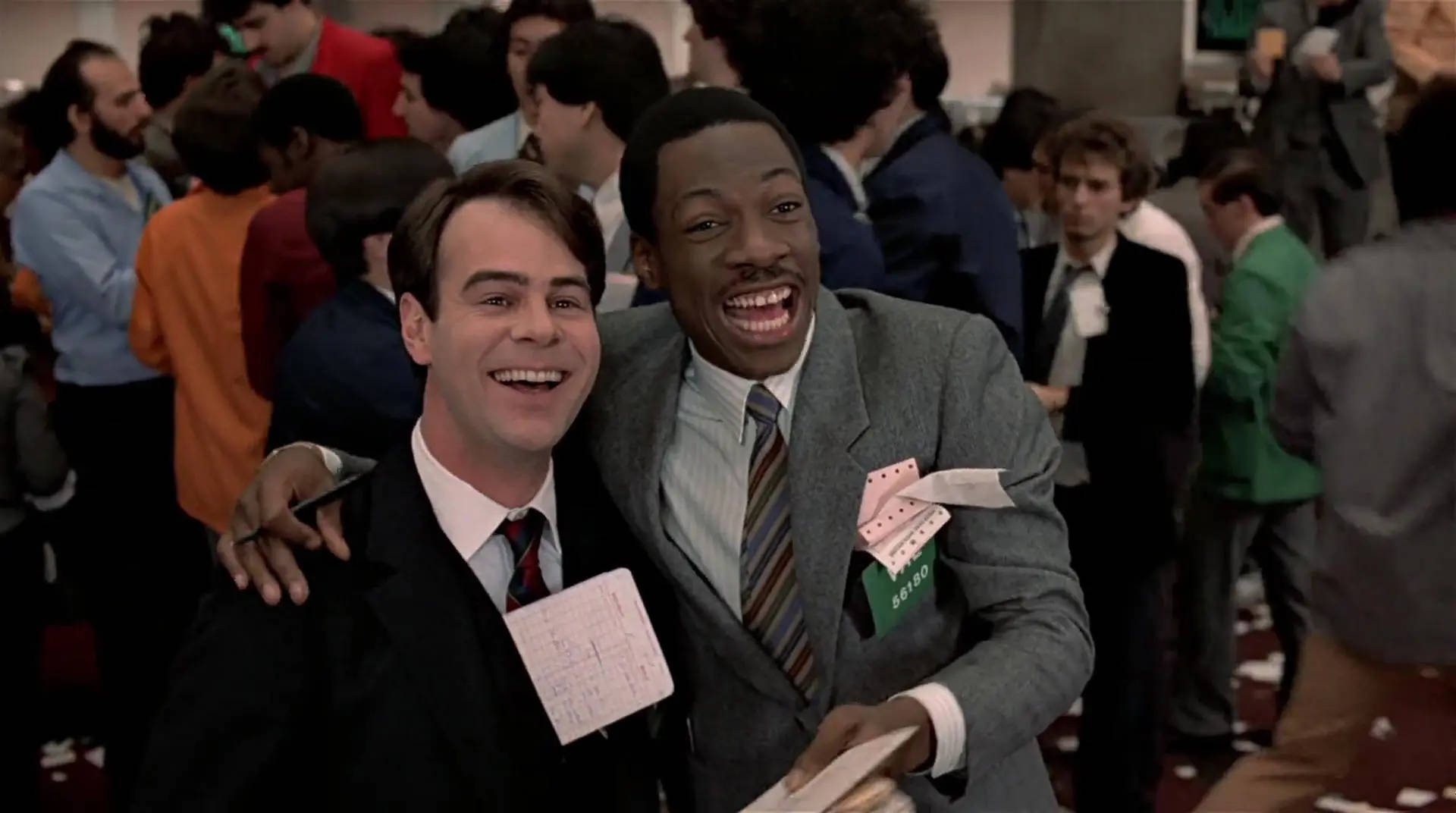 Peripeteia in Film. Definition, Meaning & Examples 9 Louis Winthorpe III and Billy Ray Valentine smile and hug in a busy trading floor while holding paper trading slips.
