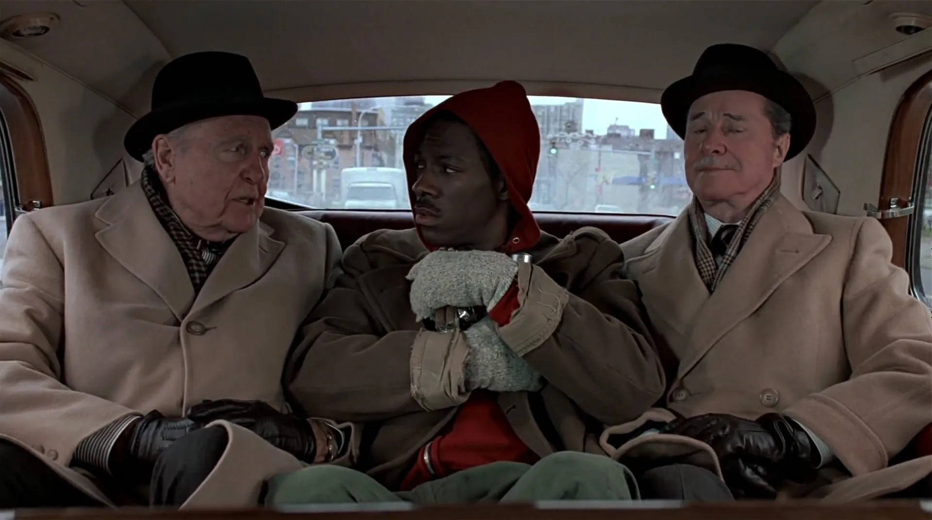 Peripeteia in Film. Definition, Meaning & Examples 5 Billy Ray Valentine sits in the back seat of a car between two older men in coats and hats while they talk to him.