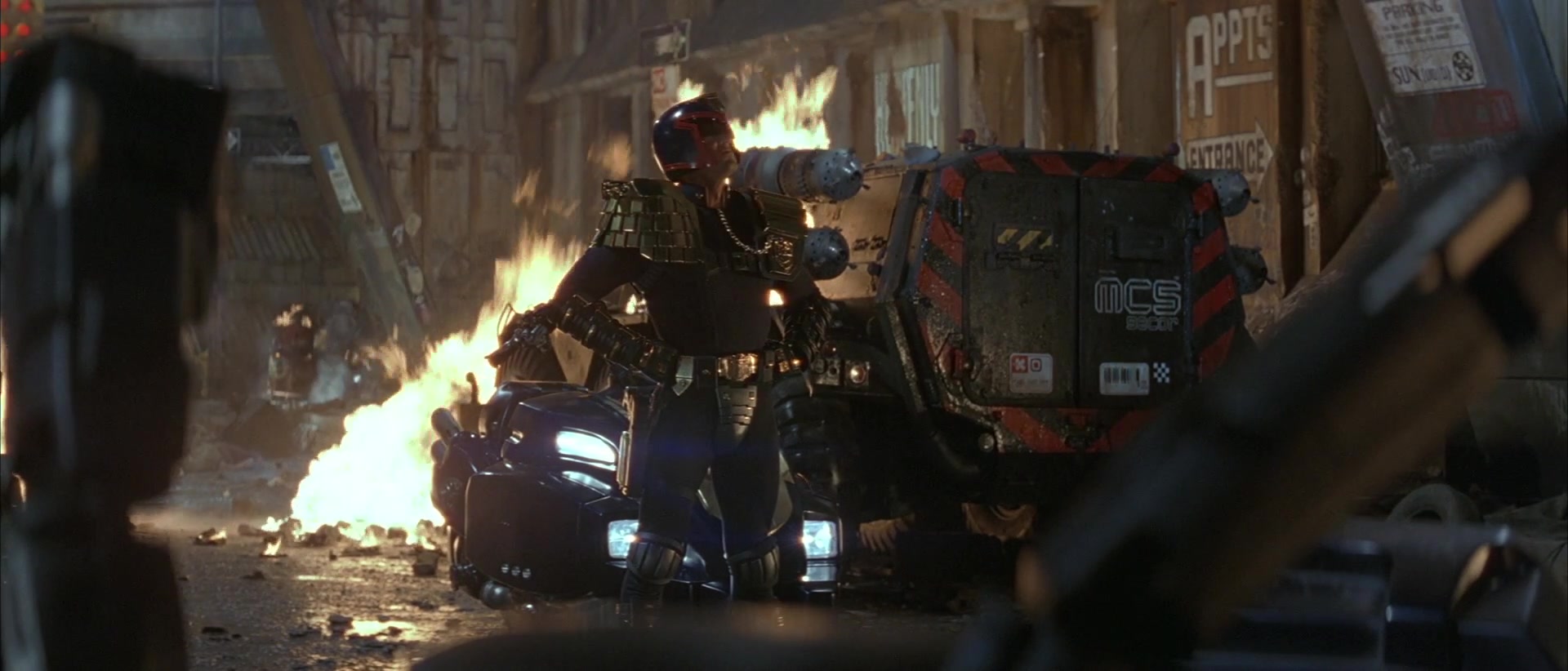 What is Cyberpunk in Film? Definition and Examples 7 Judge Dredd walks through a burning city street filled with rubble, neon signs, and wrecked vehicles.