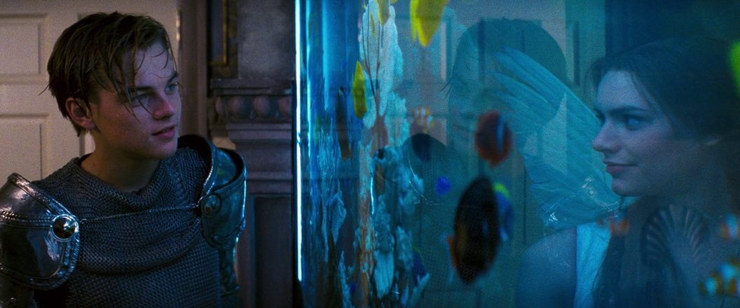 What is Anachronism? Meaning & Examples from Film 3 Romeo and Juliet meet for the first time through a fish tank, dressed in costume at a party. The scene is visually split by the glass and bright tropical fish.