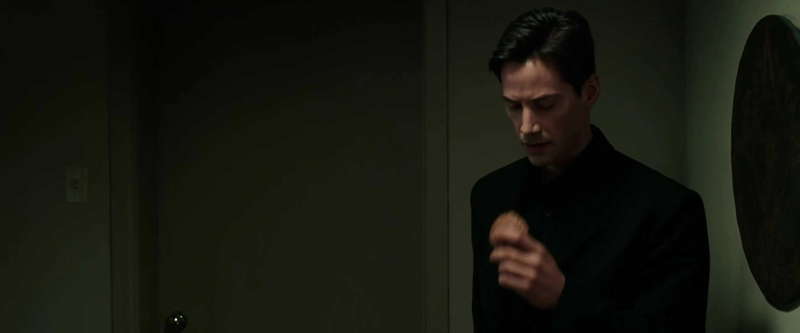 What Is an Archetype? Definition & Clear Film Examples 2 Neo stands in a dim hallway wearing a black coat, looking down while holding a fortune cookie in his hand.