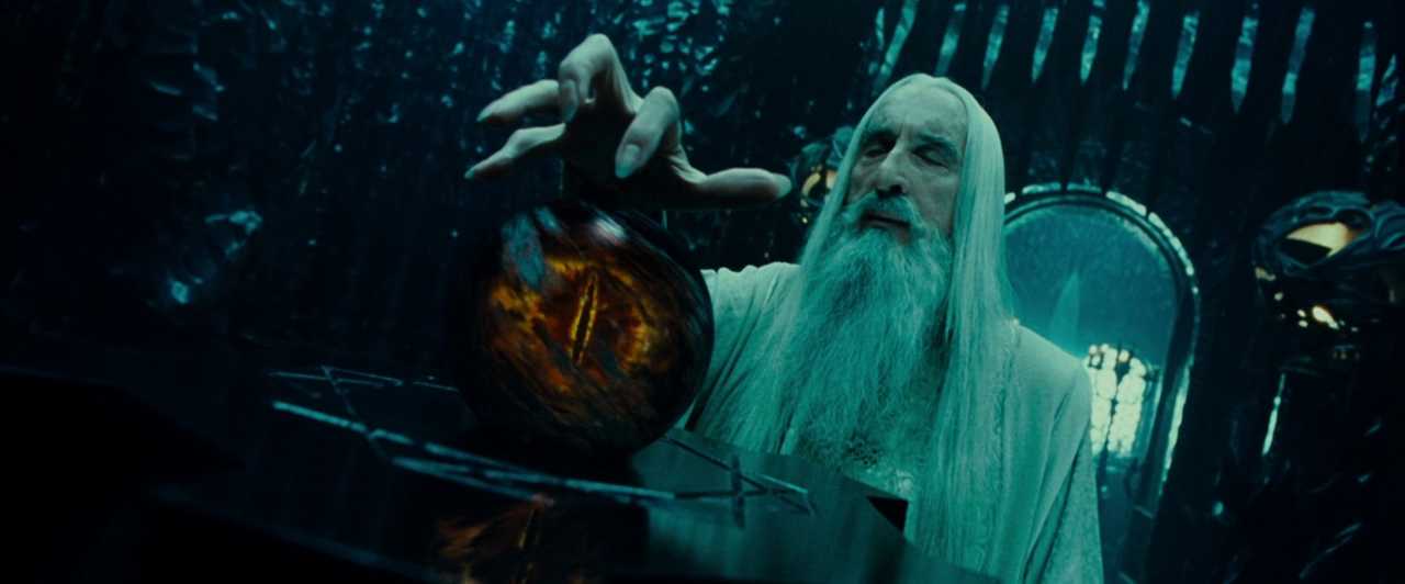 What is Fantasy in Film? Fantasy Genres Explained 3 Saruman, a white-robed wizard with long white hair and beard, reaches toward a glowing seeing-stone with the Eye of Sauron inside