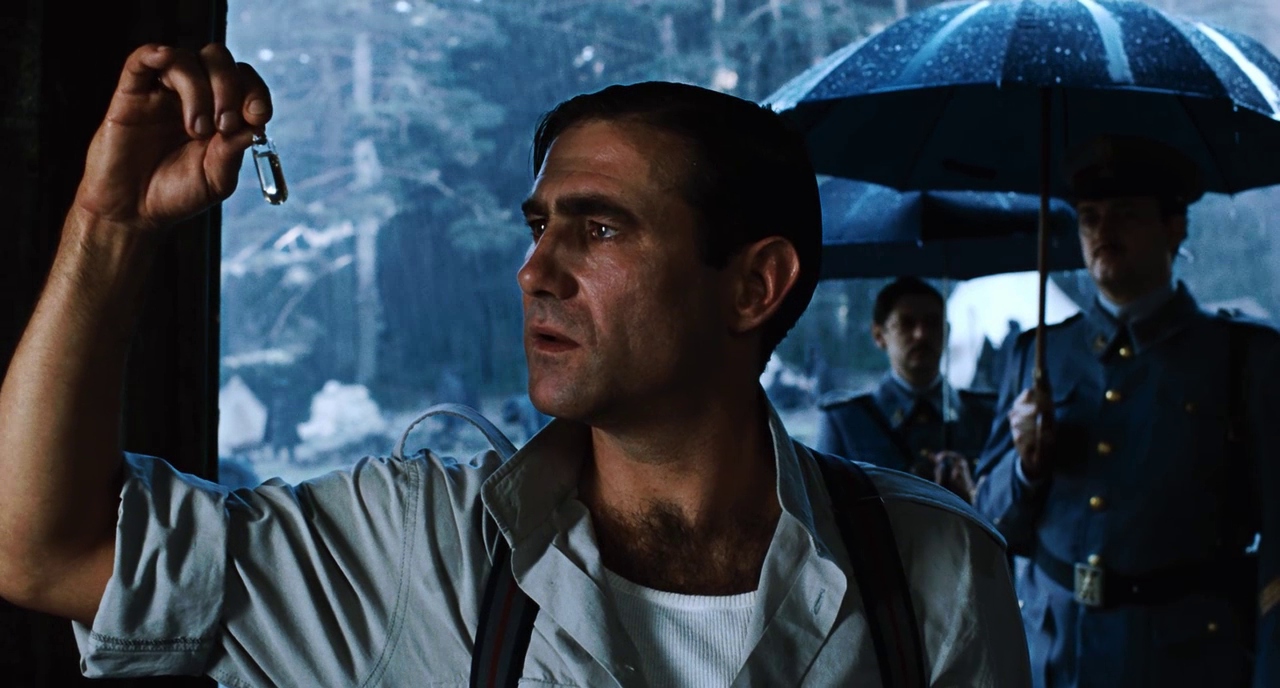 What is Fantasy in Film? Fantasy Genres Explained 4 A man in a military-style shirt holds a small glass vial while standing in front of soldiers with umbrellas in the rain