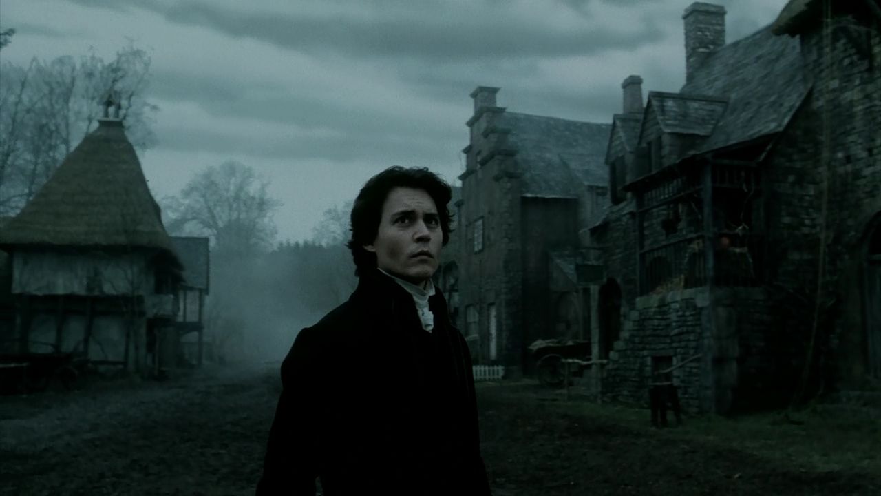 What is Fantasy in Film? Fantasy Genres Explained 7 A man in dark 18th-century clothing stands in a misty, old village with stone and timber houses under a cloudy sky