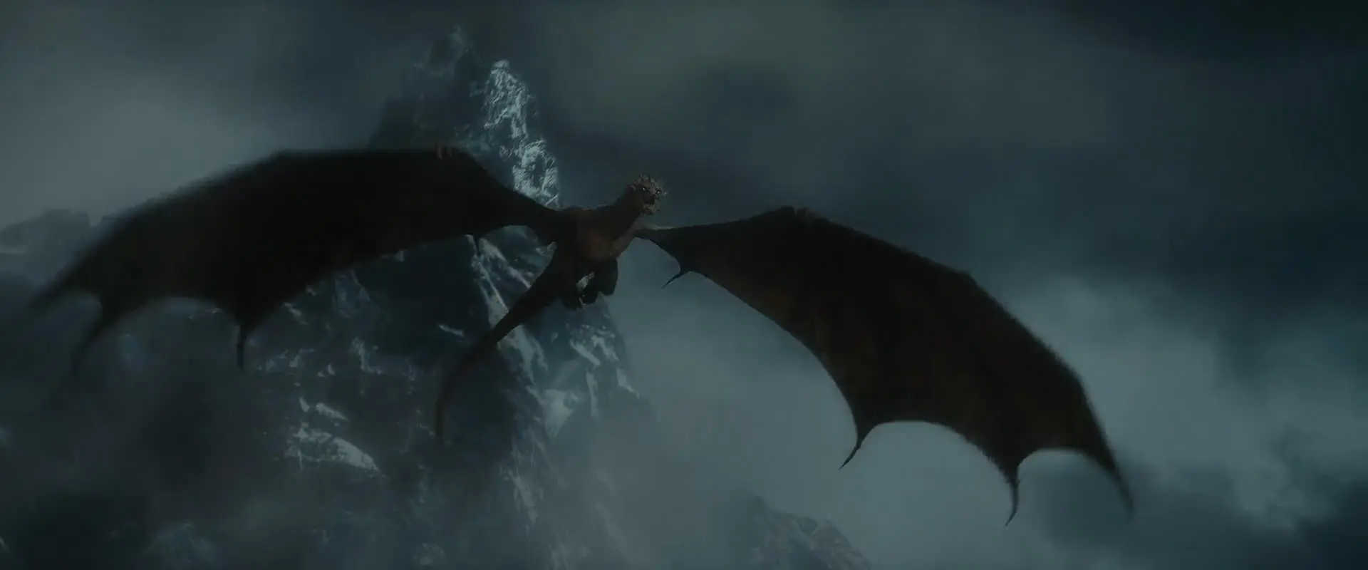 What is Fantasy in Film? Fantasy Genres Explained 2 A dragon with outstretched wings flies in front of a snowy mountain peak under dark storm clouds