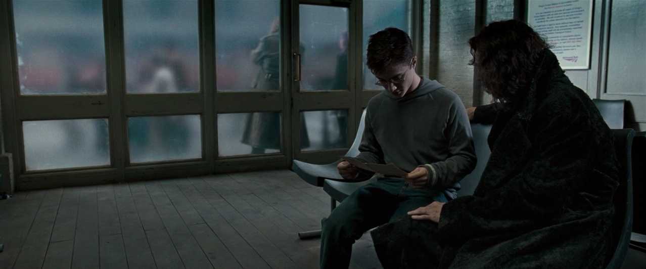 What is Fantasy in Film? Fantasy Genres Explained 5 Harry Potter and Sirius Black sit on plastic chairs in a dull, real-world train station with fogged glass doors behind them.
