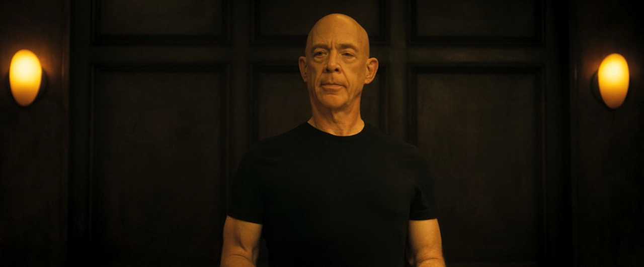 What is a Static Character? Definition & Film Examples 5 Terence Fletcher stands centered against a dark wall, wearing a black T-shirt, with warm wall lights on both sides.