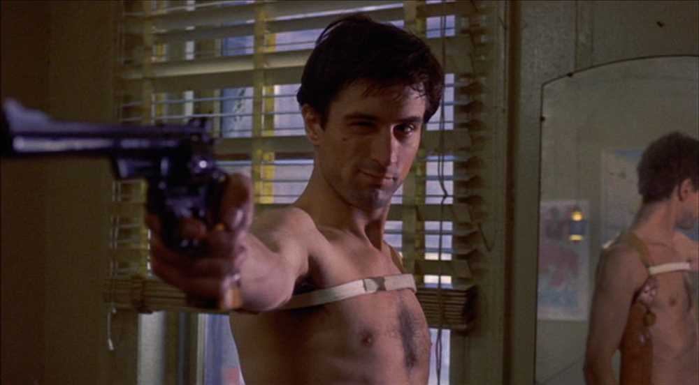 What is Characterization? Elements Defining Your Characters 9 Travis, shirtless with a shoulder holster strap, points a handgun toward the camera in a dim apartment with blinds behind him.