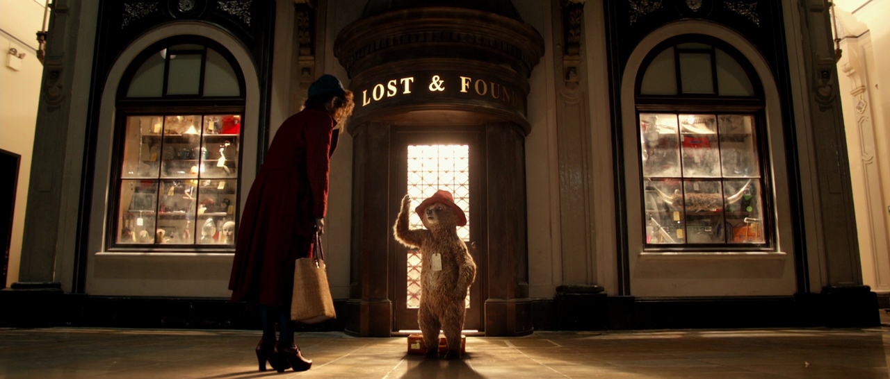 What is Characterization? Elements Defining Your Characters 4 Paddington, a small bear in a red hat with a tag on his coat, stands under a “Lost & Found” sign at a train station while a woman leans toward him.