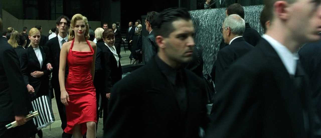 What is Verisimilitude in Film? Definition, Types & Examples 5 Neo and Morpheus stand in a crowded courtyard as people in dark suits move around them near a large fountain.