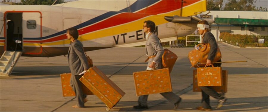 Guide: Best Wes Anderson Movies (For Filmmakers to Learn From) 3 Three suited men walk barefoot with matching luggage toward a small plane in The Darjeeling Limited