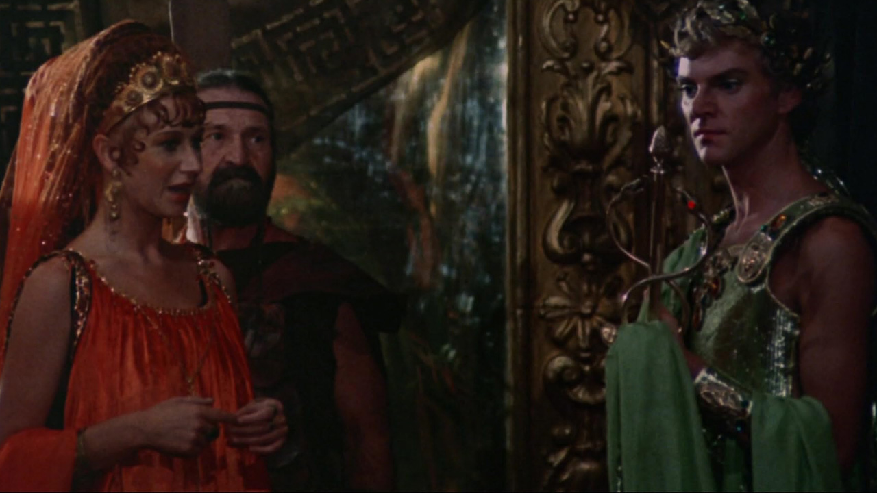 Best Tinto Brass Movies (& Why You Should Watch Them) 4 A man in a green Roman costume stares ahead while holding a scepter. To his left, a woman in a bright orange dress and veil speaks beside a bearded man in armor. The ornate background includes gold and dark red tones.