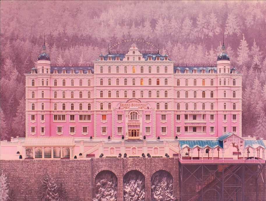 Guide: Best Wes Anderson Movies (For Filmmakers to Learn From) 12 A symmetrical, pink hotel building framed against a pastel forest in The Grand Budapest Hotel