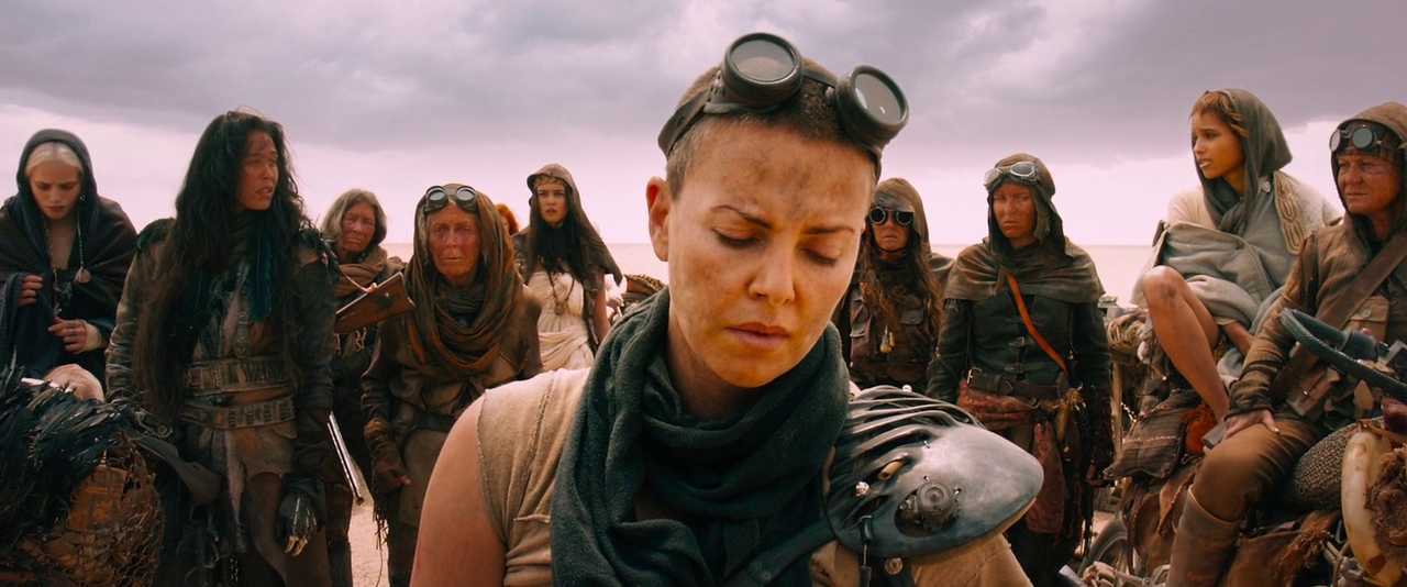 What is a Costume Designer? Role, Duties & Visual Storytelling 2 Group of women wearing worn, post-apocalyptic clothing and goggles, with Furiosa in the foreground looking down