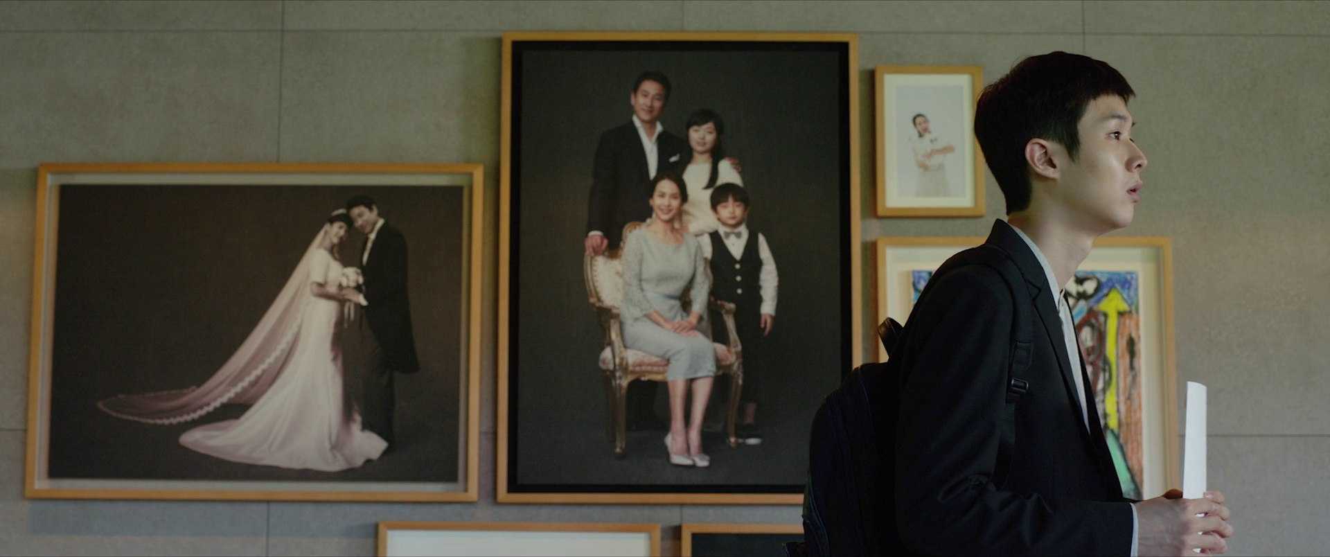 Film Theory: Definition, Discourses, and How to Use It 9 A young man in a suit stands near framed family portraits on a wall in Parasite