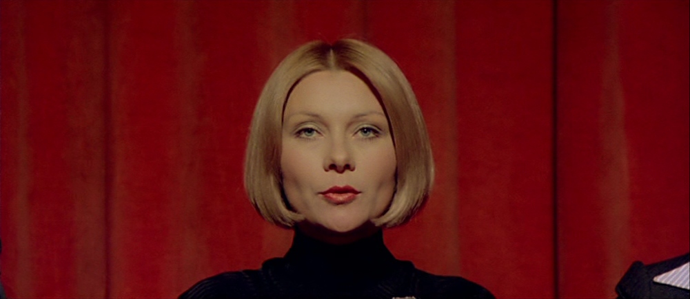 What Are Giallo Films? Definition, History & Key Examples 9 Woman in black centered against a bright red curtain in Deep Red (1975)