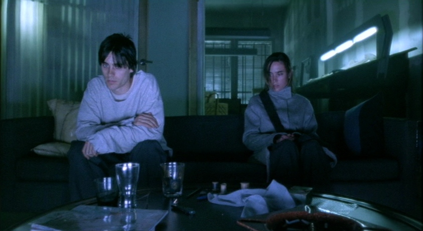 What Is Drama? Definition, Subgenres, and Themes 3 Scene from Requiem for a Dream (2000) showing two distant characters sitting on a couch in a cold, blue-lit room
