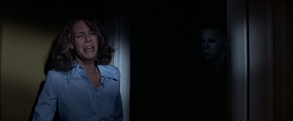 What Is a Horror Movie? Definition, Subgenres & Examples 10 Woman screaming as a masked killer watches from the shadows in Halloween (1978)
