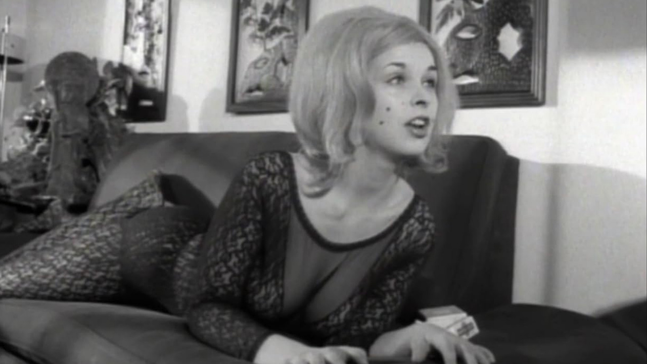 What Is Exploitation Cinema? Definition & Key Examples 14 A woman in a see-through lace outfit lies on a couch, speaking with expressive body language in Bad Girls Go to Hell (1965).