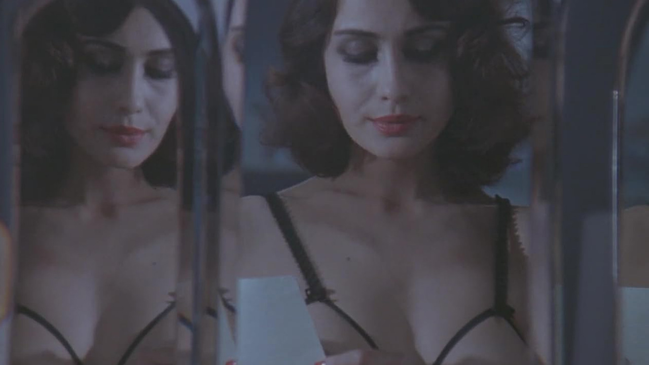 Sex, Power, and Rebellion: Symbolism in Tinto Brass Movies 3 Woman in lingerie looking at a photo while surrounded by mirror reflections, suggesting self-exploration and growing confidence in a dimly lit bedroom.