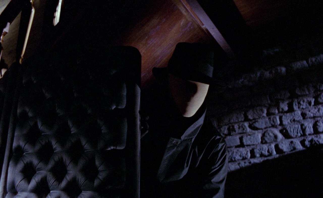 What Are Giallo Films? Definition, History & Key Examples 5 Masked figure in a black coat and hat hiding in a dark room in Blood and Black Lace (1964)