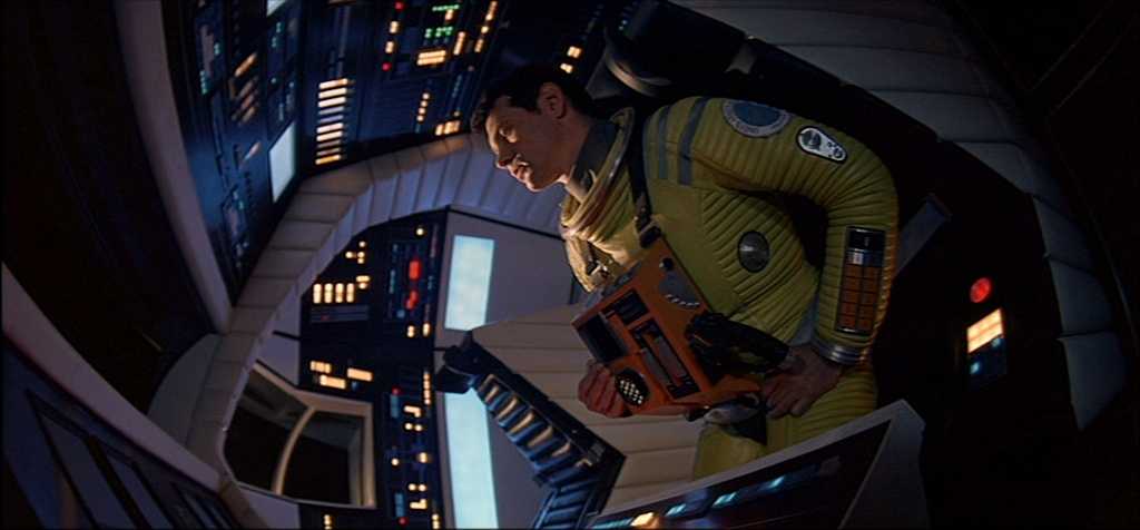 Similarities & Differences Between Science Fiction & Fantasy in Film Explained 2 Astronaut Dave Bowman in a yellow space suit inside a futuristic spaceship control room