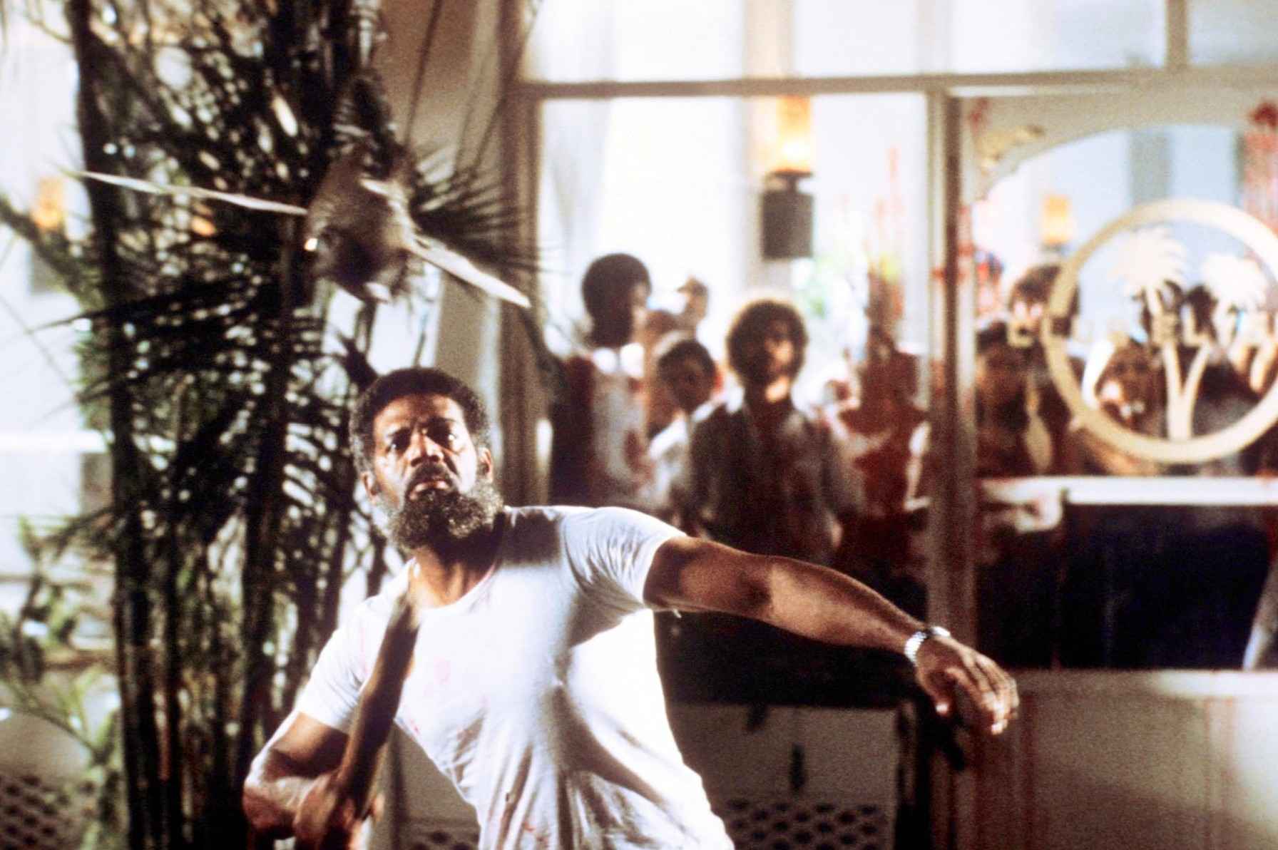 What Is a B-Movie? Definition & Film History 8 Man in a white shirt swings a weapon at a flying piranha inside a hotel as people watch from behind glass doors.