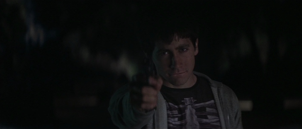 Cult Classic Films: What Makes a Movie a Cult Hit? 7 Donnie, wearing a skeleton shirt, points a gun in the dark during a tense scene from Donnie Darko (2001).