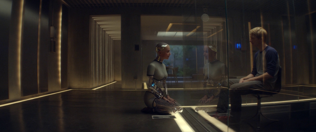 Similarities & Differences Between Science Fiction & Fantasy in Film Explained 8 A humanoid robot kneels on one side of a glass wall facing a seated man in a futuristic room