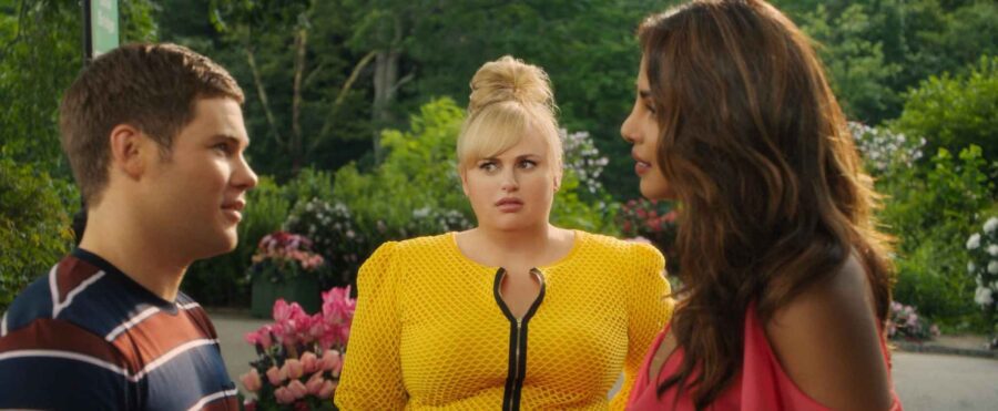 What is a Romcom? Definition, History & Tropes 10 Natalie stands between two characters in a garden in Isn't It Romantic (2019)