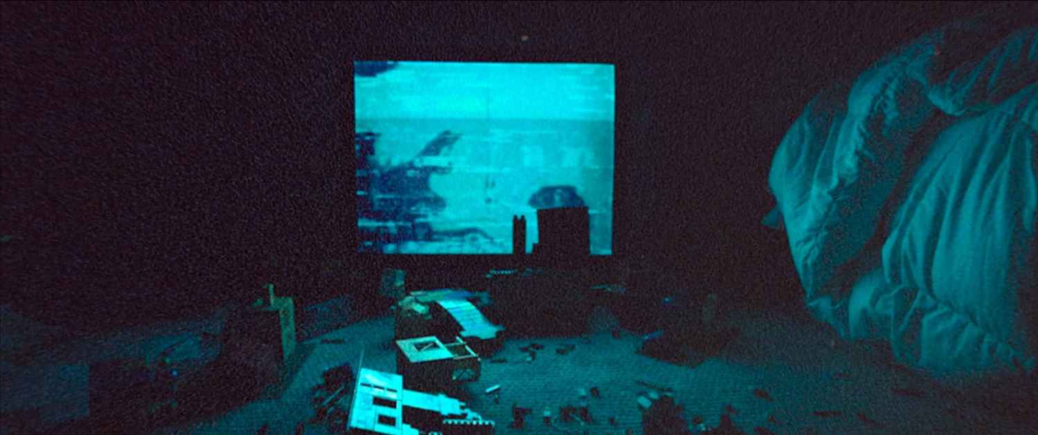 What Is Analog Horror? Definition, History & Examples 2 A grainy image of a dimly lit bedroom with a static-filled TV screen glowing blue and scattered toys on the floor